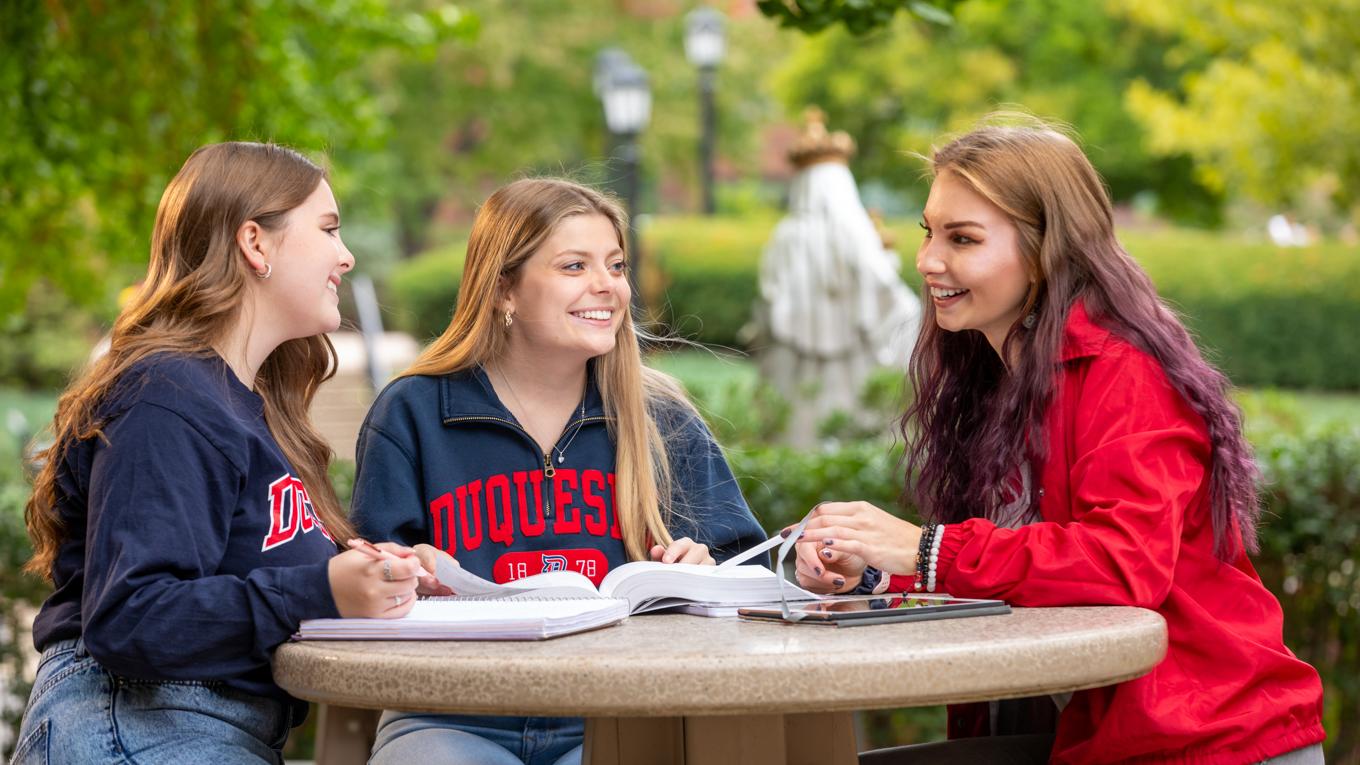 Three secondary education students studying around table outside