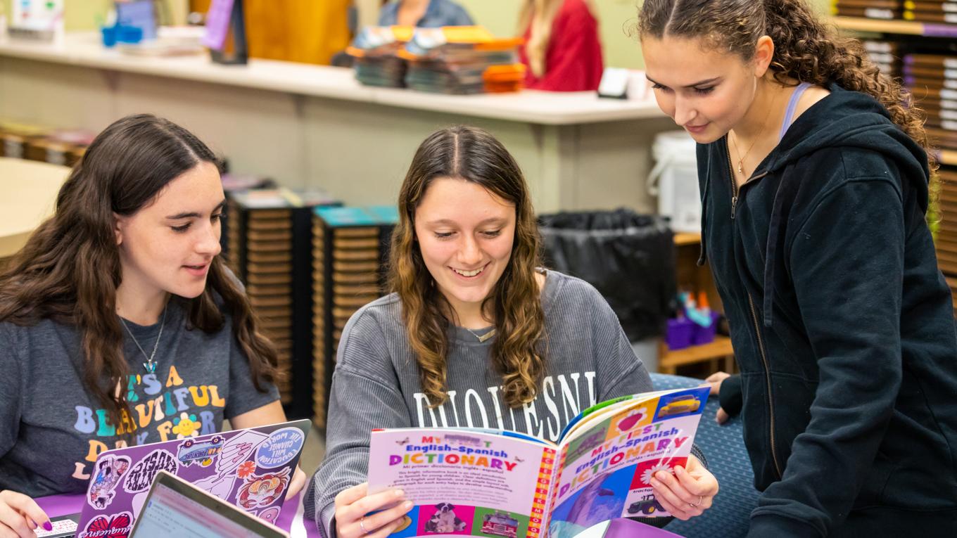Three special education students gathered around curriculum instruction book in library learning center