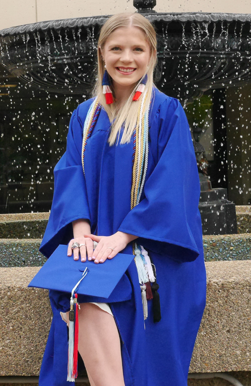 Brianna DeKlever sitting outside on fountain ledge in graduation regalia 
