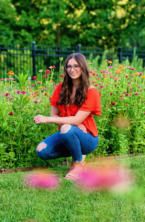 Photo of Megan Caskey kneeling between wildflowers in field and a fence behind her