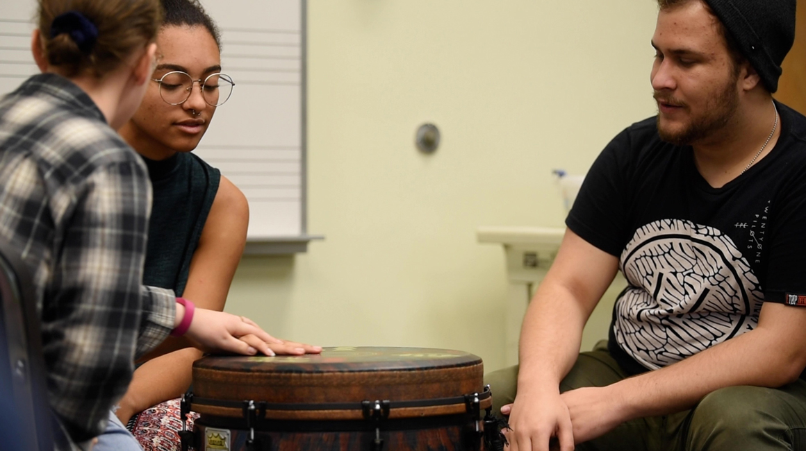 Three students working together with a drum.