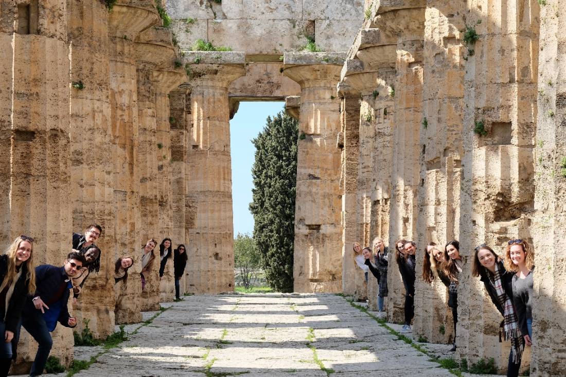 Students peek heads out behind ancient Greek temple columns.