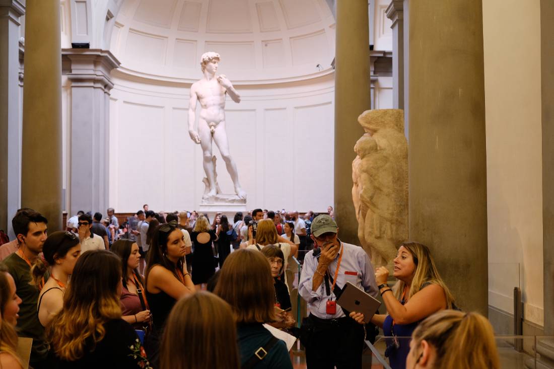 Students close together listening to guide about the statue located in the background in a museum.