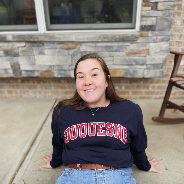 Julie poses on the ground in a Duquesne sweatshirt.